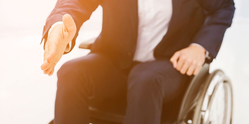 Trabajador vestido de traje esperando para estrechar la mano. Imagen impersonal de un trabajador ofreciendo su mano, sentado en silla de ruedas.