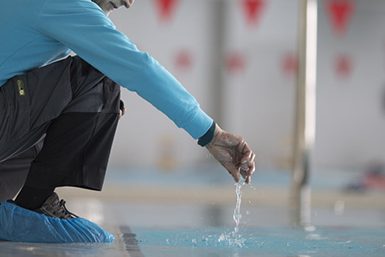Mantenimiento Vectoris Conseje agachado sobre una piscina, tomando una muestra de agua.