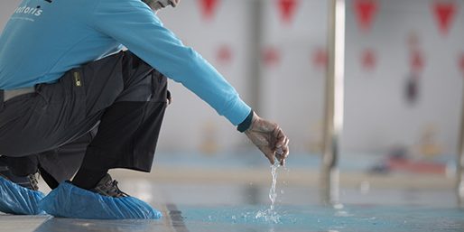 Mantenimiento Vectoris Conseje agachado sobre una piscina, tomando una muestra de agua.