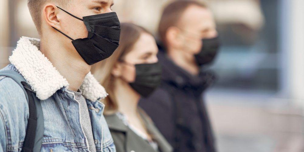 jovenes medidas anticovid Tres jóvenes con mascarillas negras mirando hacia el lado derecho.